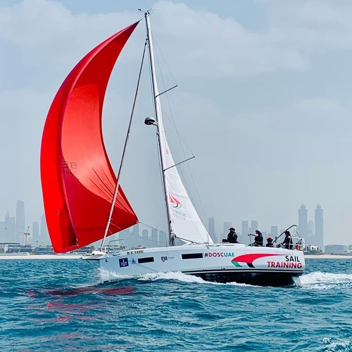 Beneteau sailing yacht under red spinnaker off Dubai, with the city skyline behind